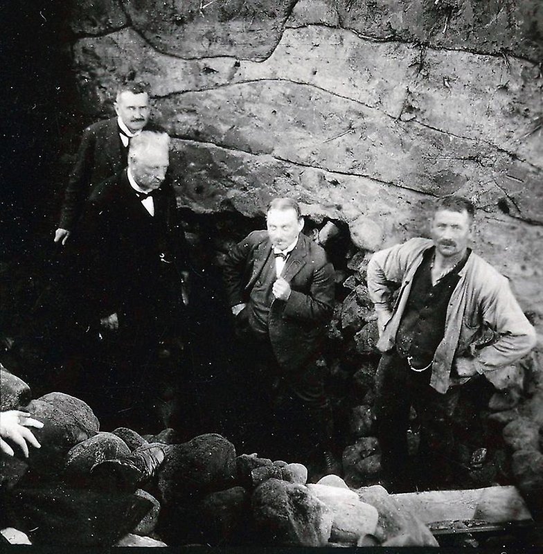 Gammalt fotografi på fyra män som står nere i en bronsåldersgrav.