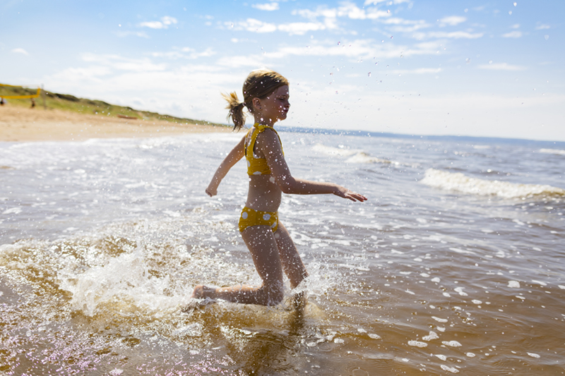 En flicka springer ut i havet för att bada. I bakgrunden syns en sandstrand. 